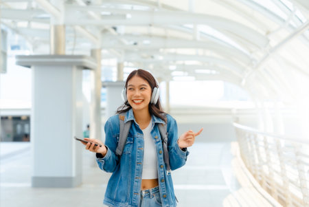 Young asian woman using headphone for listening nice music and walking in city. Girl happiness, smile face. Female love listen music that make her relax and enjoying lifeの写真素材