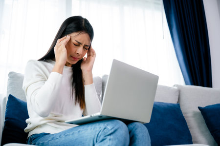 Office syndrome. Overworked tired young asian woman feeling headache, having eyesight problem after computer laptop work. Stressed young woman suffering from fatigue at homeの写真素材