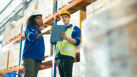 Smiling workers in distribution warehouse having a cheerful conversation. They wearing vest and safety helmet in workの写真素材
