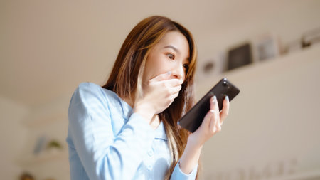 Funny euphoric young asian woman celebrating winning or getting ecommerce shopping offer on mobile smartphone. Excited happy girl winner looking smart phone celebrating successの写真素材