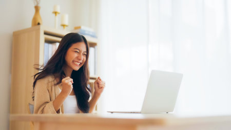 Funny euphoric young asian woman celebrating winning or getting ecommerce shopping offer on computer laptop. Excited happy girl winner looking at notebook celebrating successの写真素材