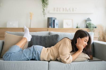 Happy young asian woman relax on comfortable couch at home texting messaging on smartphone, smiling girl use cellphone, browse wireless internet on gadget, shopping online from homeの写真素材