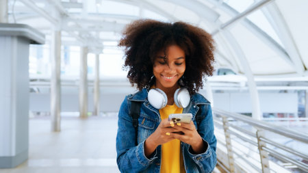 Happy young afro woman listening to playlist music with wireless headphones while wearing yellow shirt and jeans jacket outdoorの写真素材