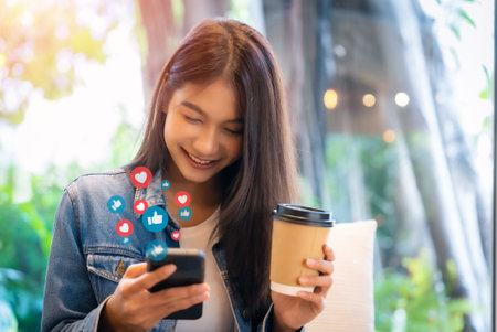 Young asian women watching live streaming video in a cafe coffee shop. Happy female using mobile smartphone social media application for entertainmentの写真素材