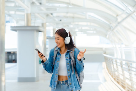 Young asian woman using headphone for listening nice music and walking in city. Girl happiness, smile face. Female love listen music that make her relax and enjoying lifeの写真素材