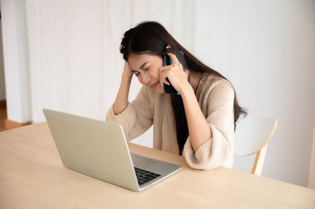 Young asian woman talking mobile smartphone while working on computer laptop at house. Work at home, Video conference, Video callingの写真素材