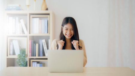 Funny euphoric young asian woman celebrating winning or getting ecommerce shopping offer on computer laptop. Excited happy girl winner looking at notebook celebrating successの写真素材