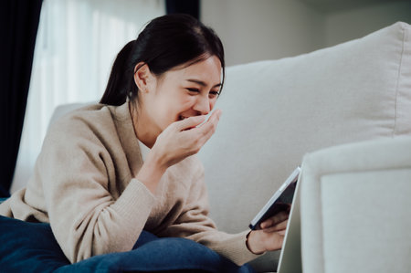 Happy young asian woman relax on comfortable couch at home texting messaging on smartphone, smiling girl use cellphone, browse wireless internet on gadget, shopping online from homeの写真素材