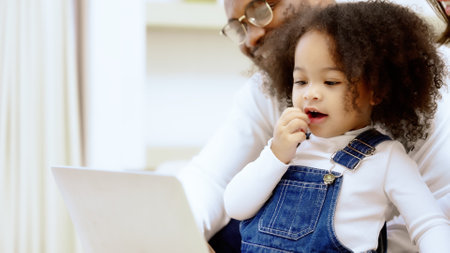 Happy african family parents and little children enjoy using computer laptop together sit on sofa, technology addicted couple with kids having fun at homeの写真素材