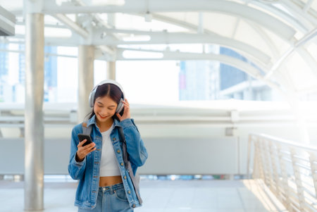 Young asian woman using headphone for listening nice music and walking in city. Girl happiness, smile face. Female love listen music that make her relax and enjoying lifeの写真素材