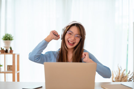 Funny euphoric young asian woman celebrating winning or getting ecommerce shopping offer on computer laptop. Excited happy girl winner looking at laptop celebrating successの写真素材
