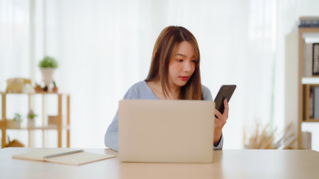 Young asian woman happy working on computer laptop and hand typing chat message on mobile smartphone at home. Video call, Online meetingの写真素材