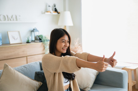 Happy teen asian girl blogger smiling face waving hand talking to webcam recording vlog, social media influencer streaming, making video call at home. She thumb up good or betterの写真素材