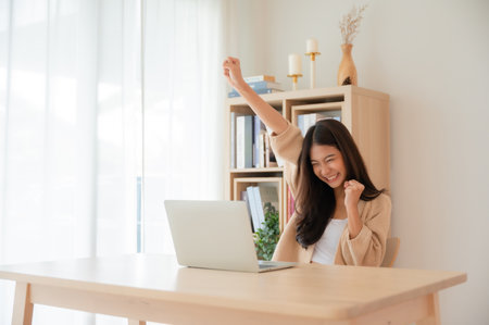 Happy euphoric young asian woman celebrating winning or getting ecommerce shopping offer on computer laptop. Excited happy girl winner looking at notebook celebrating successの写真素材