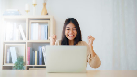 Funny euphoric young asian woman celebrating winning or getting ecommerce shopping offer on computer laptop. Excited happy girl winner looking at notebook celebrating successの写真素材