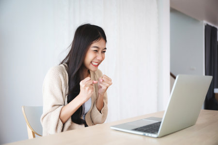 Funny euphoric young asian woman celebrating winning or getting ecommerce shopping offer on computer laptop. Excited happy girl winner looking at notebook celebrating successの写真素材