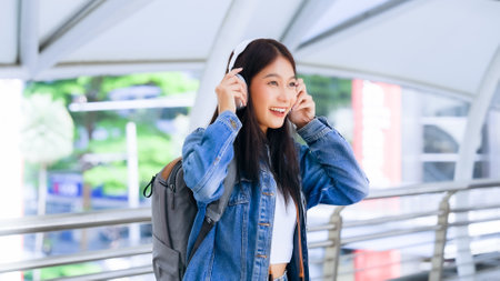 Portrait of happy young asian woman listening music online with wireless headphones from a smartphone in the cityの写真素材