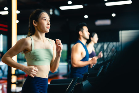 Fit young woman and man running on a treadmill during a workout class at fitness gym