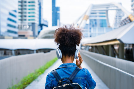 Back view of black student girl wearing headset and using mobile smartphone, Walking at college building outdoor, Happy and smiling woman teenager. Modern educationの写真素材