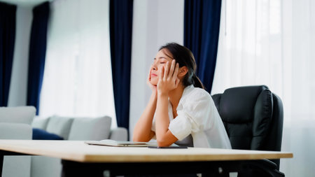 Bored young asian woman sitting at her workplace at home, boring expression is thinking of somethingの写真素材