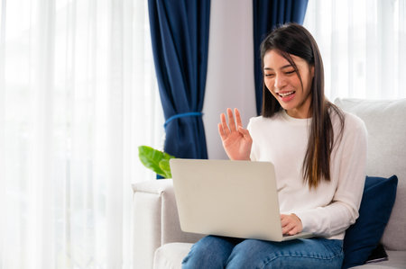 Young asian woman working on her laptop at home, grinning. attractive Asian woman utilizing computer for online schooling, video calling, and conference callsの写真素材