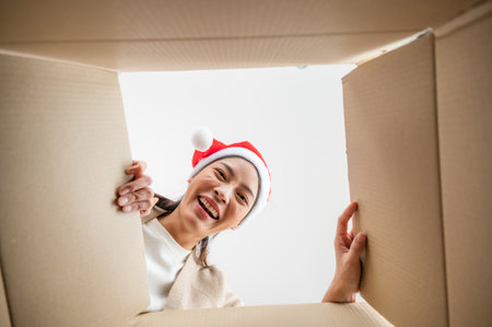 Happy young asian woman wearing christmas hat and unpacking gift box. Beautiful female smiling and surprised while opening present and looking inside. Happy new year, Merry christmas and Thankgiving conceptの写真素材