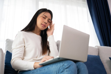 Office syndrome. Overworked tired young asian woman feeling headache, having eyesight problem after computer laptop work. Stressed young woman suffering from fatigue at homeの写真素材