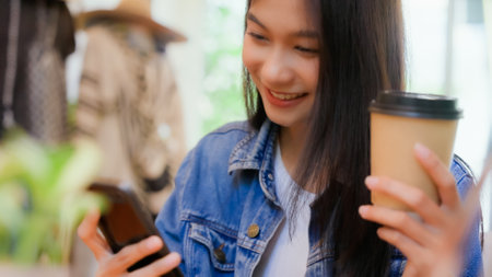 Asian woman happy and typing messages on smartphone in cafe Smiling young woman sitting at table with hot cup of coffee and using mobile phoneの写真素材