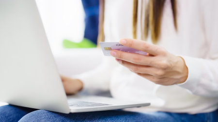 Young asian woman sitting on sofa in living room, makes online banking payments through the internet from bank card on computer laptop. Shopping online on notebook with credit cardの写真素材