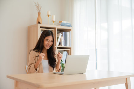 Happy euphoric young asian woman celebrating winning or getting ecommerce shopping offer on computer laptop. Excited happy girl winner looking at notebook celebrating successの写真素材