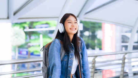 Portrait of happy young asian woman listening music online with wireless headphones from a smartphone in the cityの写真素材
