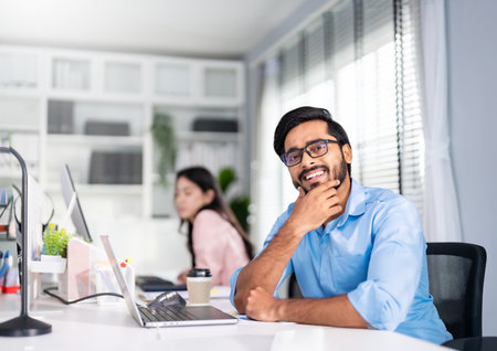 Indian professional business man, businessman wearing glasses working on computer, looks directly at camera and smiles friendlyの写真素材