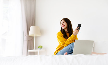 Morning Time in Bedroom Young Asian Woman Happy Working on Computer Laptop, Sitting on Bed at Houseの写真素材