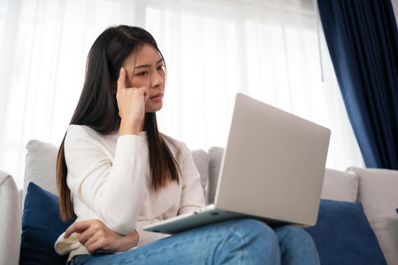 Young asian woman working on computer laptop on couch in living room at homeの写真素材