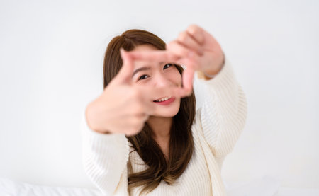Young asian woman happy and making frame with fingers on white background in houseの写真素材