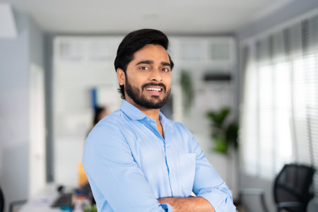 Portrait of formal business man confident successful. Indian businessman or manager in light blue shirt, stands at workplace in office, arms crossed, looks directly at camera and smiles friendlyの写真素材