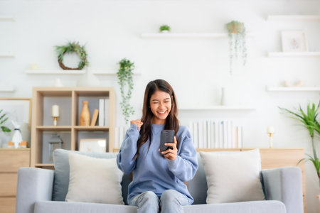 Happy young asian woman relax on comfortable couch at home texting messaging on smartphone, smiling girl use cellphone, chatting online message, shopping online from homeの写真素材