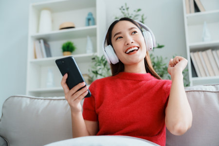 Young Asian woman relaxing on sofa at home, listening music with headset on cell phone. People lifestyle conceptの写真素材
