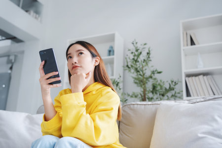 Happy young asian woman relax on comfortable couch at home texting messaging on smartphone, smiling girl use cellphone chatting, online shopping at home, video call communicationの写真素材