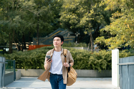 Portrait of handsome Asian student using smartphone. A young man walking outdoor happy smiling with holding mobile phoneの写真素材