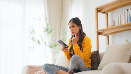 Happy young asian woman relax on comfortable couch at home, typing chat message on smartphone, smiling girl use cell phone chatting, searching information on browser wireless internet, online shoppingの写真素材