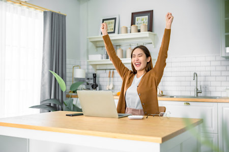 Funny euphoric young asian woman celebrating winning or getting ecommerce shopping offer on computer laptop. Excited happy girl winner looking at notebook celebrating successの写真素材