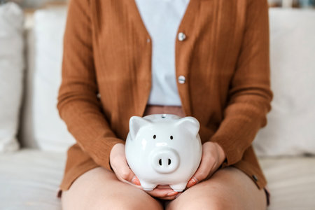 Woman hand holding piggy bank while sitting on sofa. Save money and financial investmentの写真素材
