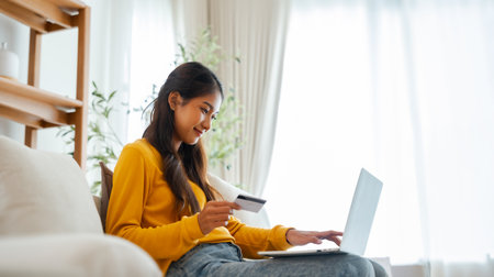 Young asian woman sitting on sofa in living room, makes online banking payments through the internet from bank card on computer laptop. Shopping online on notebook with credit cardの写真素材