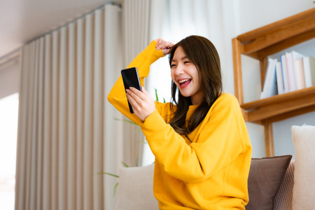 Happy young asian woman relax on comfortable couch at home texting messaging on smartphone, smiling girl use cellphone, chatting online message, shopping online from homeの写真素材