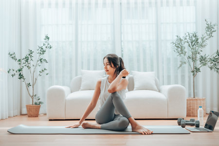 Young Asian woman stretching yoga workout on exercise mat while online training class with computer laptop in living roomの写真素材