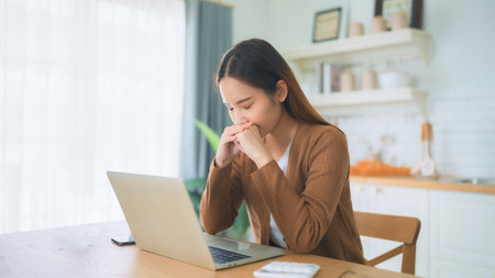 Asian young woman seriously working on computer laptop in house. She thinking find solution problem of workの写真素材