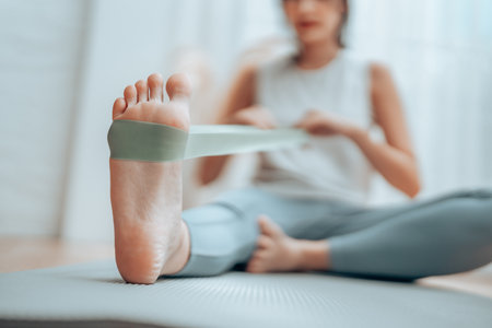 Young Asian woman doing pilates workout using elastic strap pulling with arms for shoulder training on yoga mat indoors. Resistance band exercise at homeの写真素材