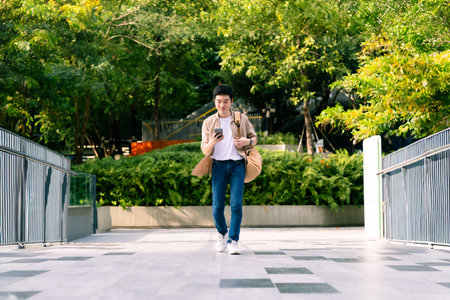 Portrait of handsome Asian student using smartphone. A young man walking outdoor happy smiling with holding mobile phoneの写真素材