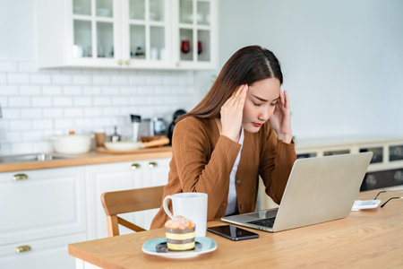 Office syndrome. Overworked tired young asian woman feeling headache, having eyesight problem after computer laptop work. Stressed young woman suffering from fatigue at homeの写真素材